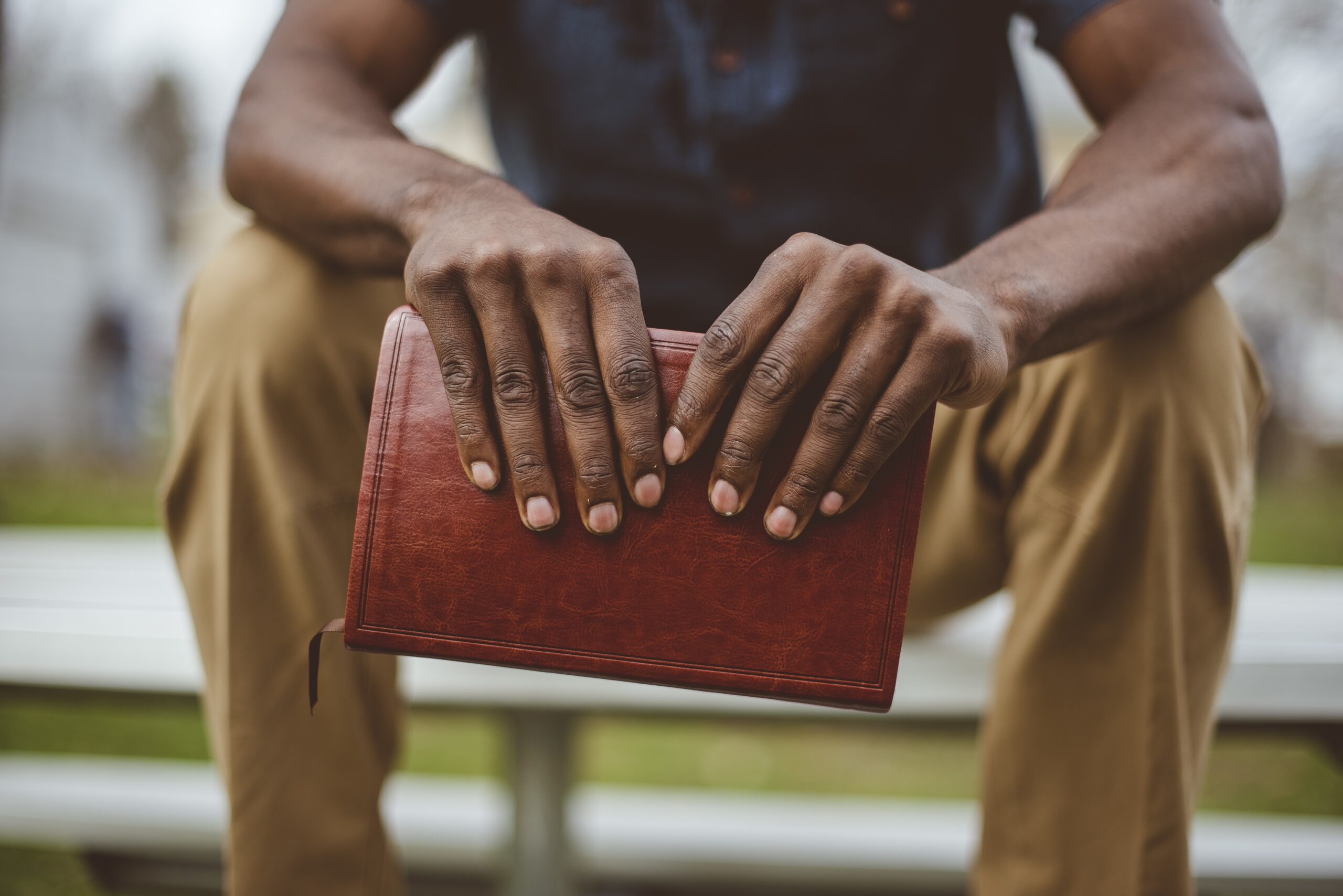 A closeup shot of a male sitting in the park while holding the bible with a blurred background