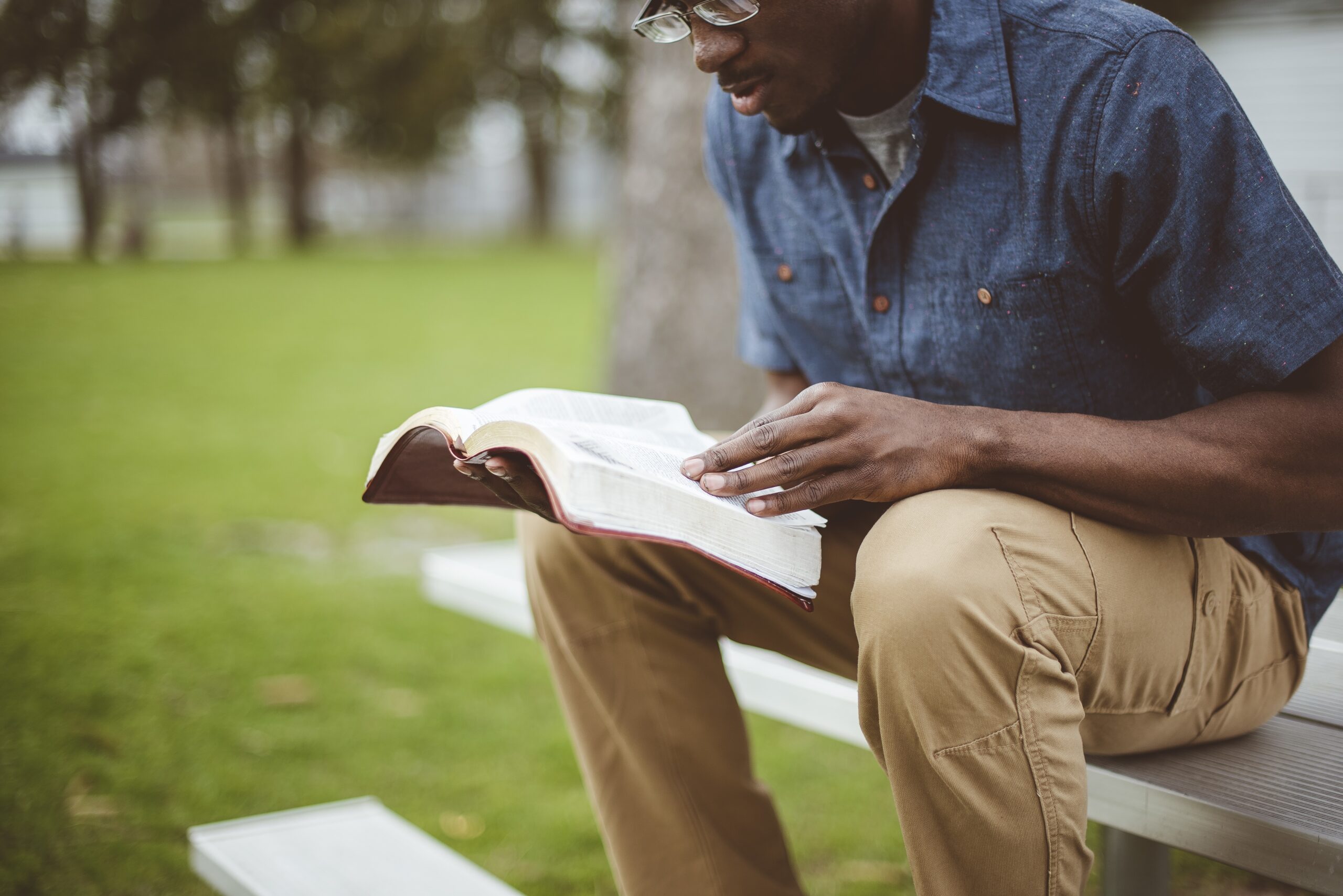 A young African-American male sitting and reading the Bible in a park